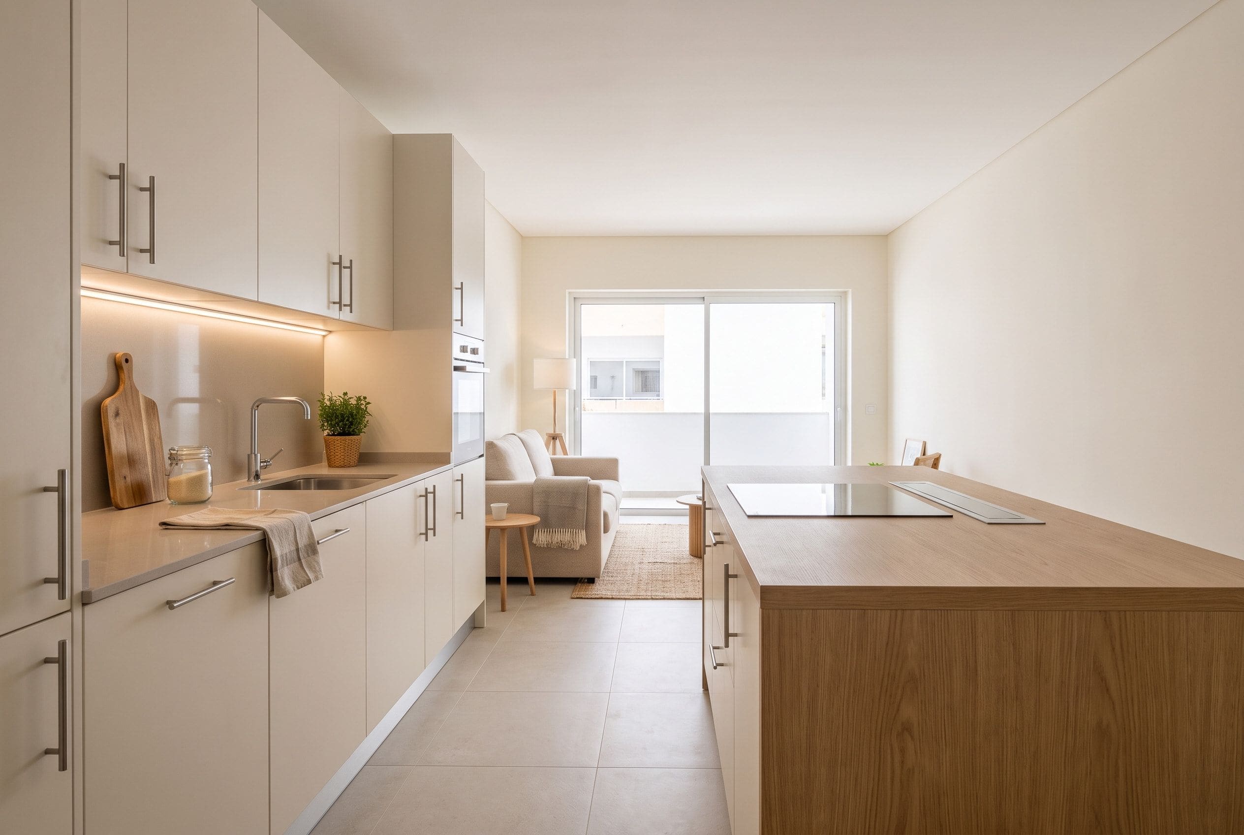 Cozinha de apartamento em Faro com frentes claras, bancada contínua e ligação aberta à zona de estar